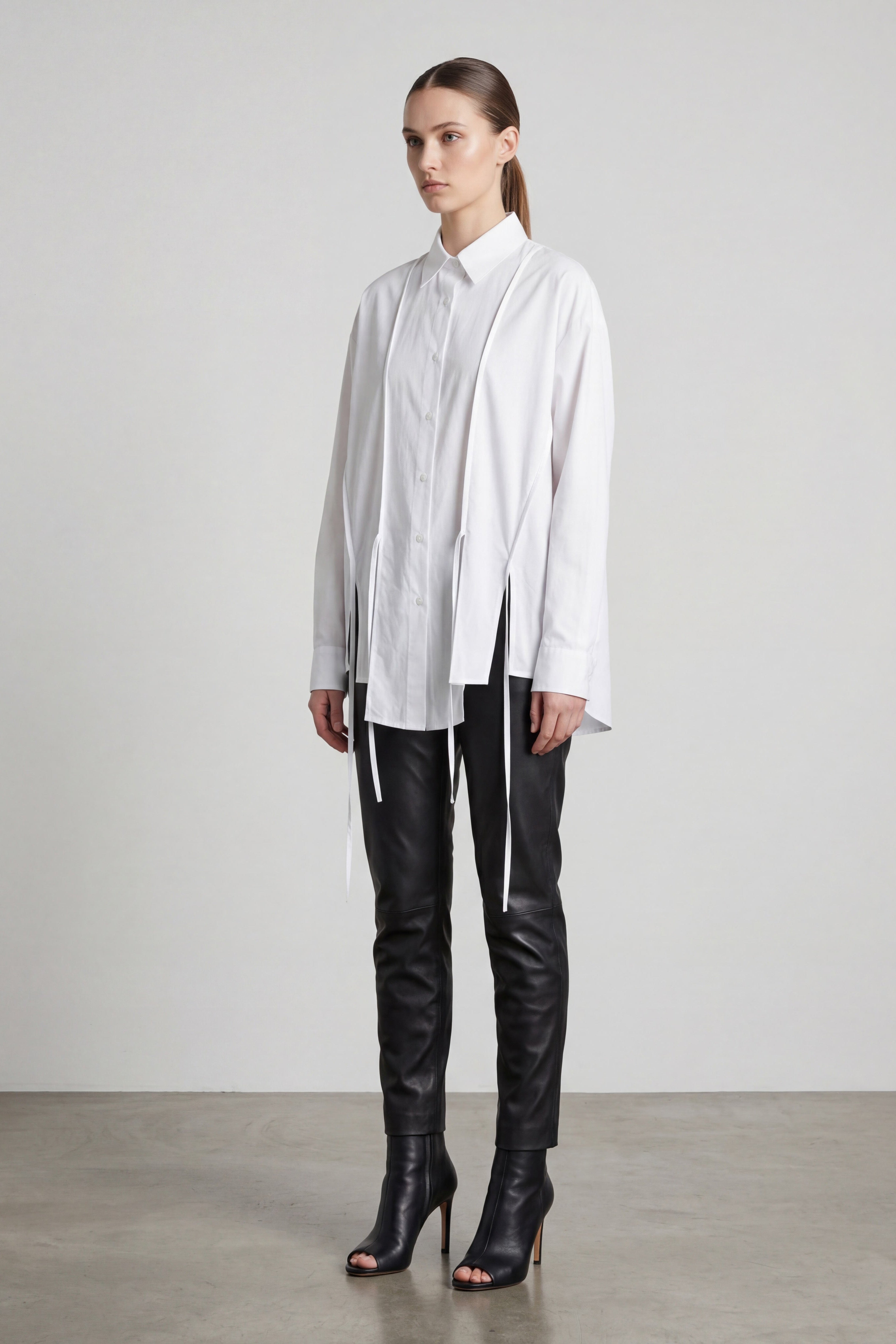 Woman wearing a white shirt and black leather pants with high heels on a plain background