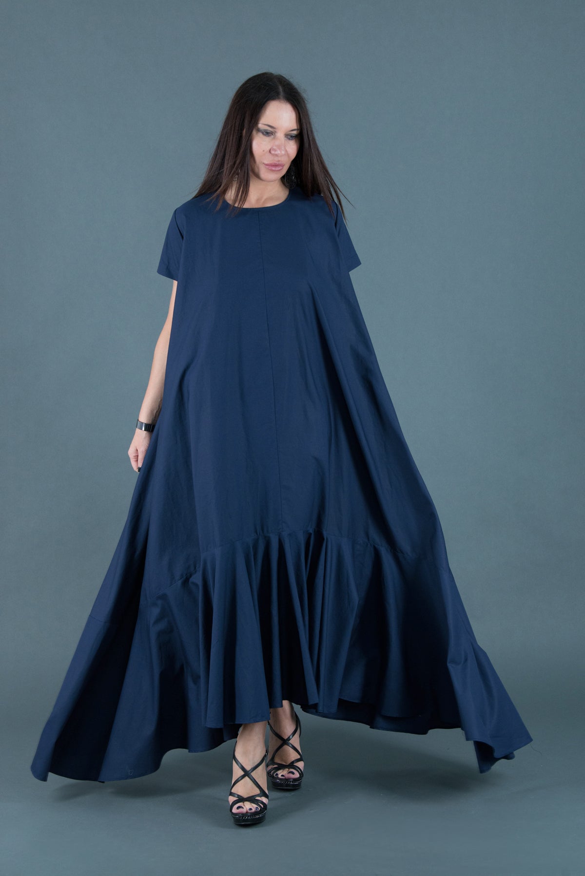 Woman wearing a long navy blue dress against a gray background