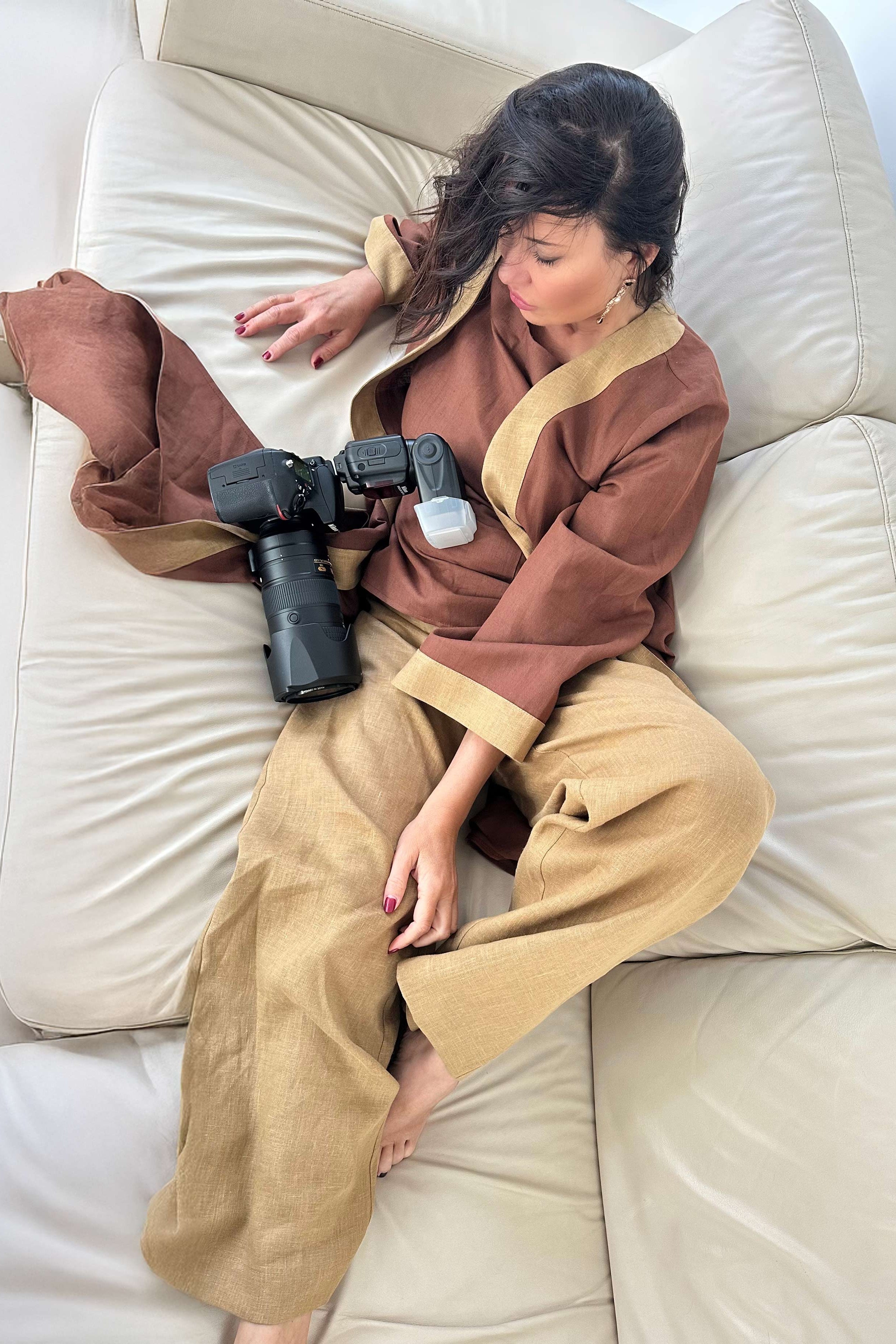 Person sitting on a beige couch holding a camera, wearing a brown and beige outfit.