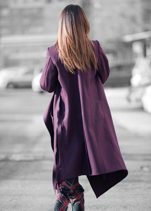 Person wearing a long purple coat walking on a street.