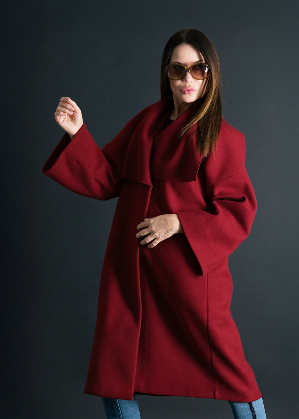 Woman wearing a red coat and sunglasses against a dark background