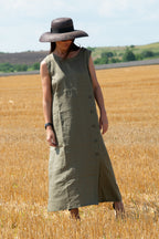 Woman in a long green linen dress and wide-brimmed hat standing in a field of golden wheat.