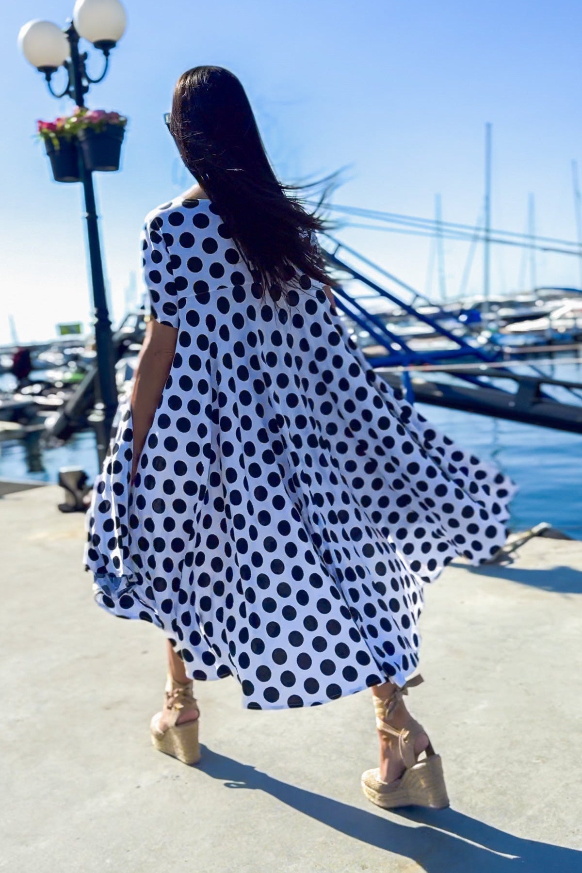 Woman in a polka dot dress standing by a marina with boats in the background
