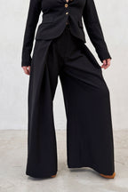 Person wearing a black suit with wide-leg pants on a light gray background