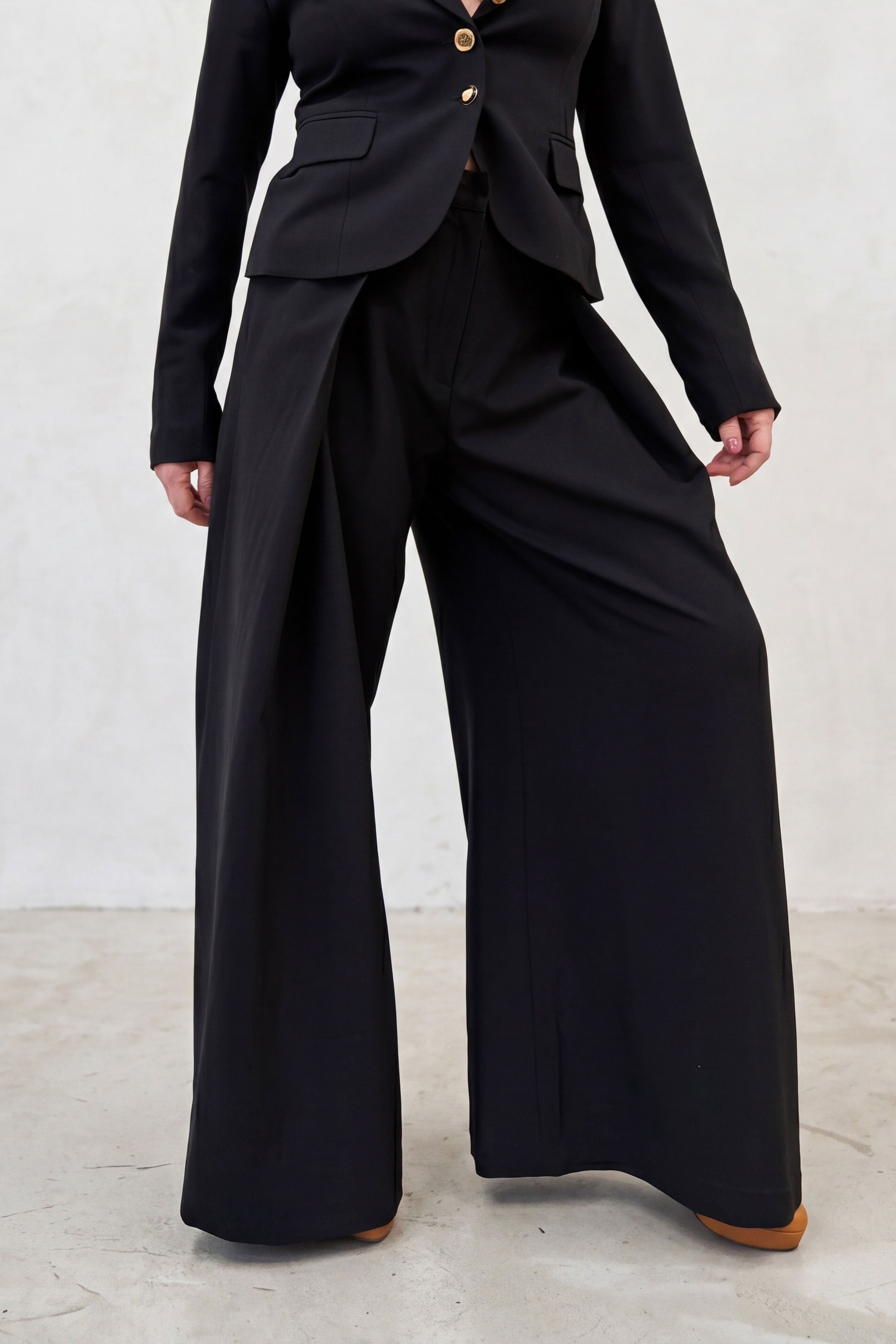 Person wearing a black suit with wide-leg pants on a light gray background