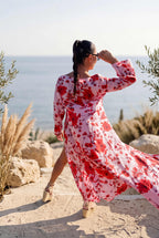 Woman in a red and white floral dress standing on a rocky beach with ocean view.