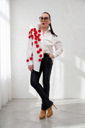 Woman wearing a white shirt with red floral details, black pants, and tan shoes in a minimalistic setting.