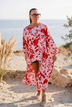 Woman wearing a red and white floral dress standing on a beach with ocean in the background