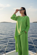 Woman in a bright green outfit standing on a boat with ocean and sky in the background