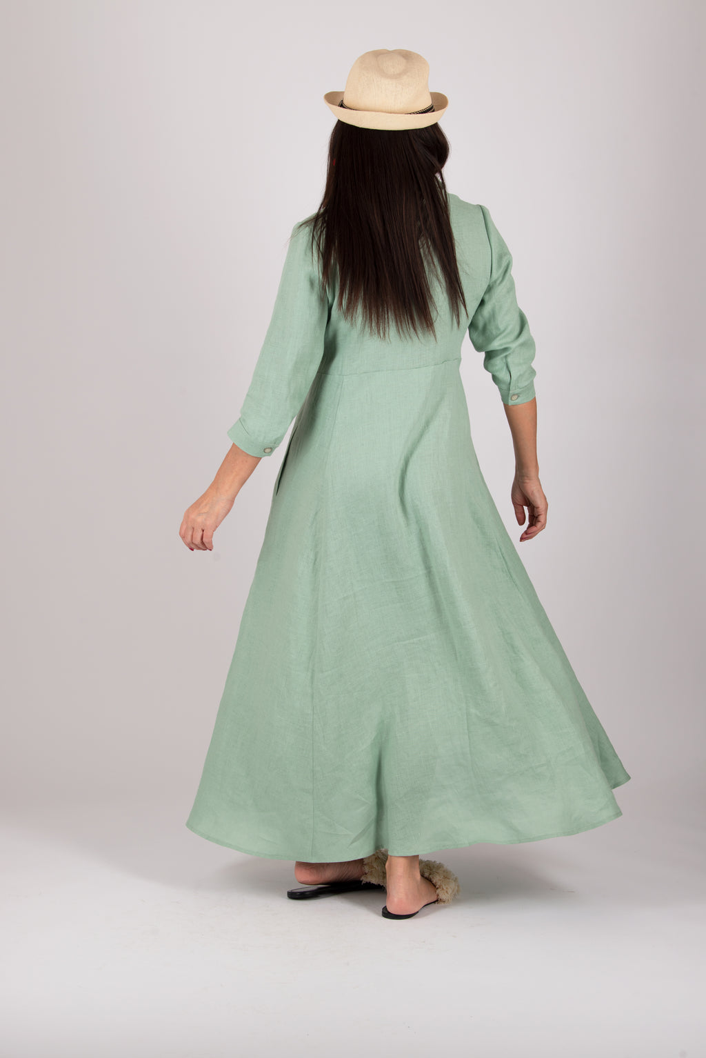 Woman wearing a long mint green dress with a hat on a plain background