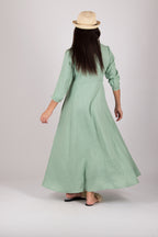 Woman wearing a long mint green dress with a hat on a plain background