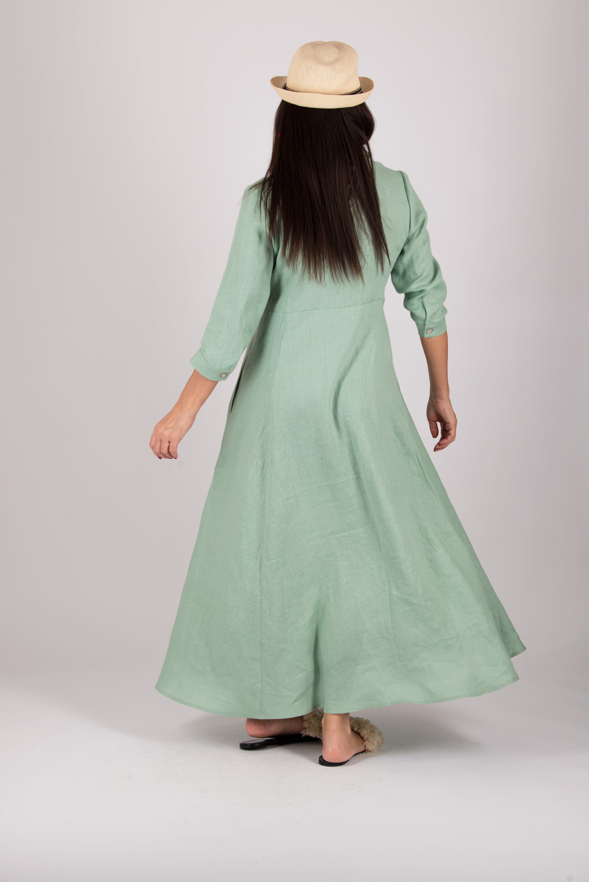 Woman wearing a long mint green dress with a hat on a plain background