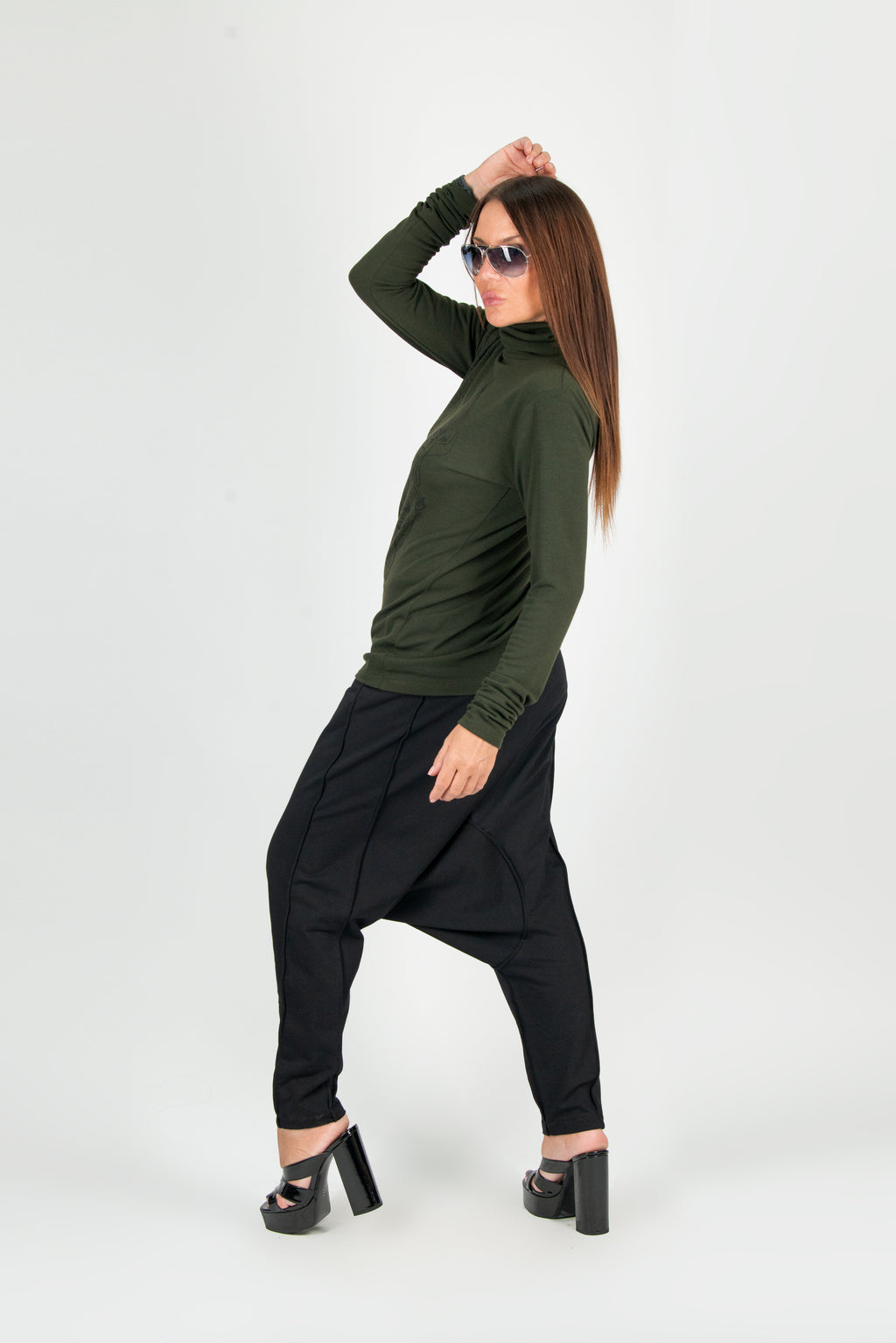 Woman wearing a green long-sleeve top and black harem pants on a white background