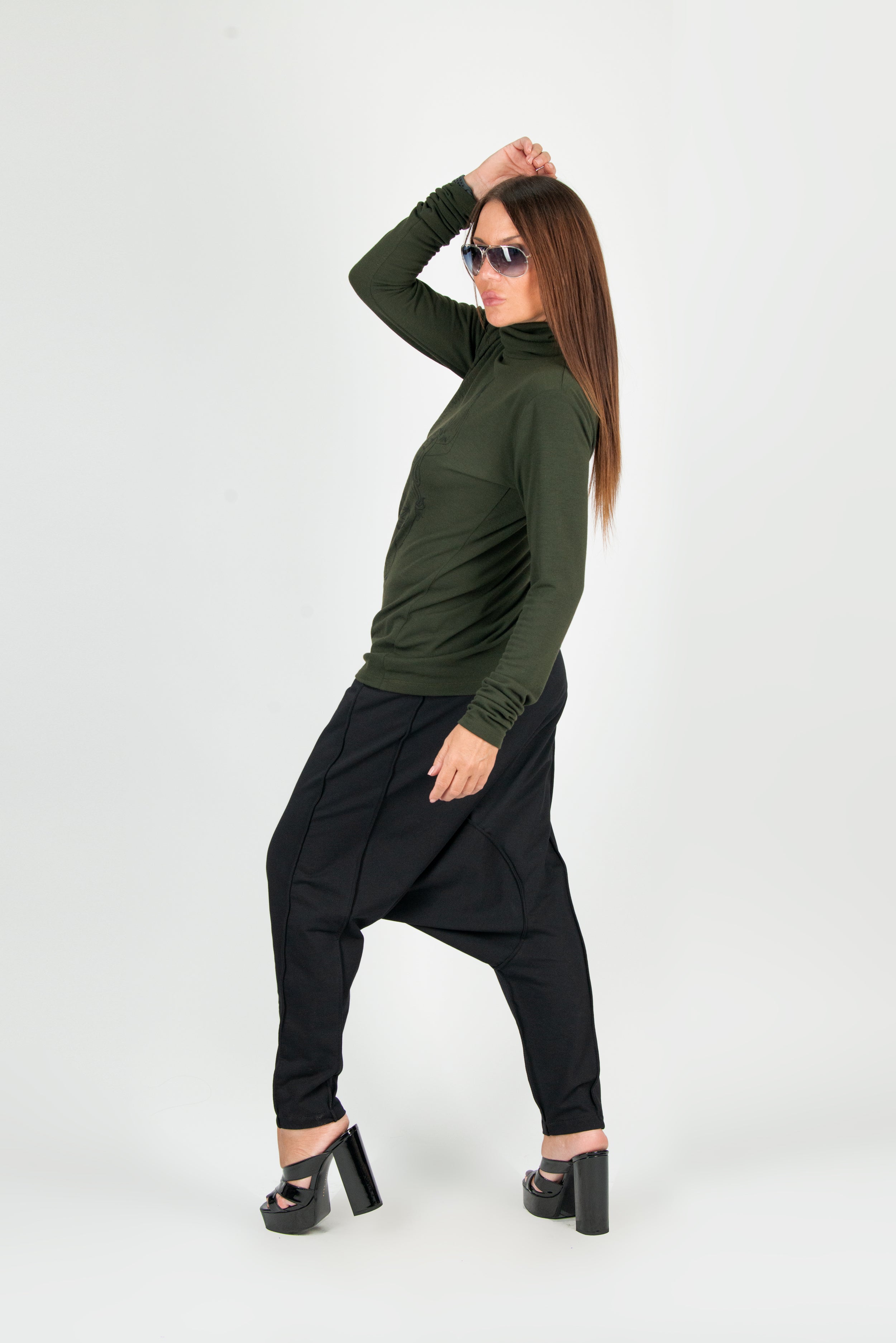 Woman wearing a green long-sleeve top and black harem pants on a white background
