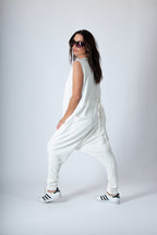 Woman wearing a white outfit with black Adidas shoes on a plain background