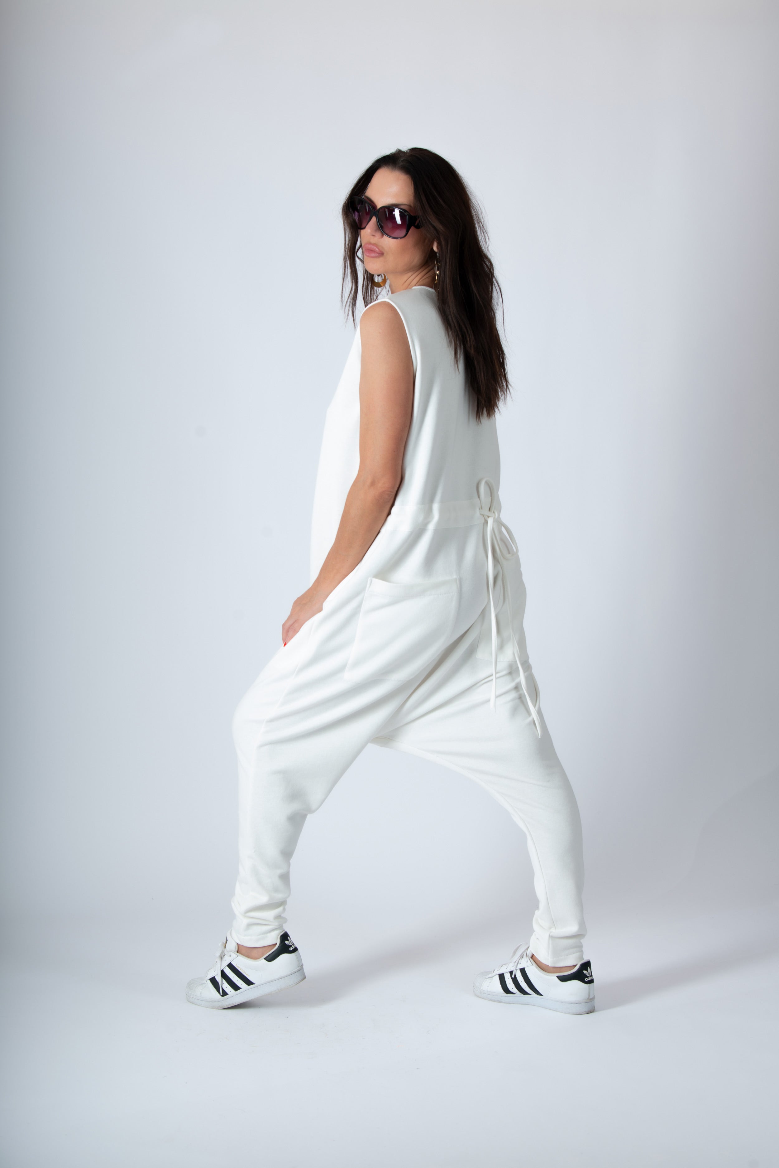 Woman wearing a white outfit with black Adidas shoes on a plain background