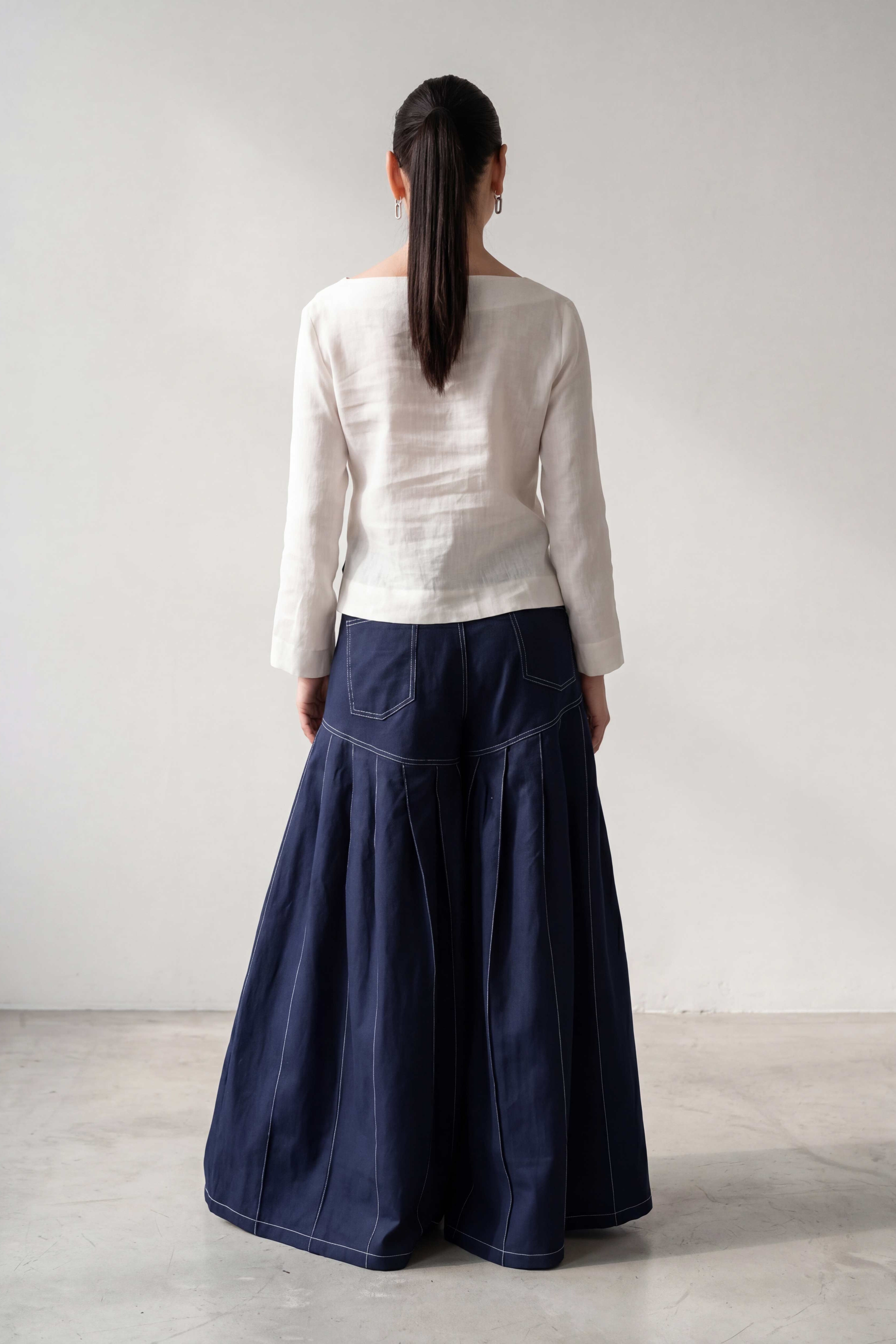 Person wearing a white top and navy blue skirt against a plain background