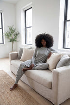 Woman sitting on a beige sofa in a bright living room with large windows.