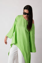Woman wearing a bright green oversized top and white pants on a plain background