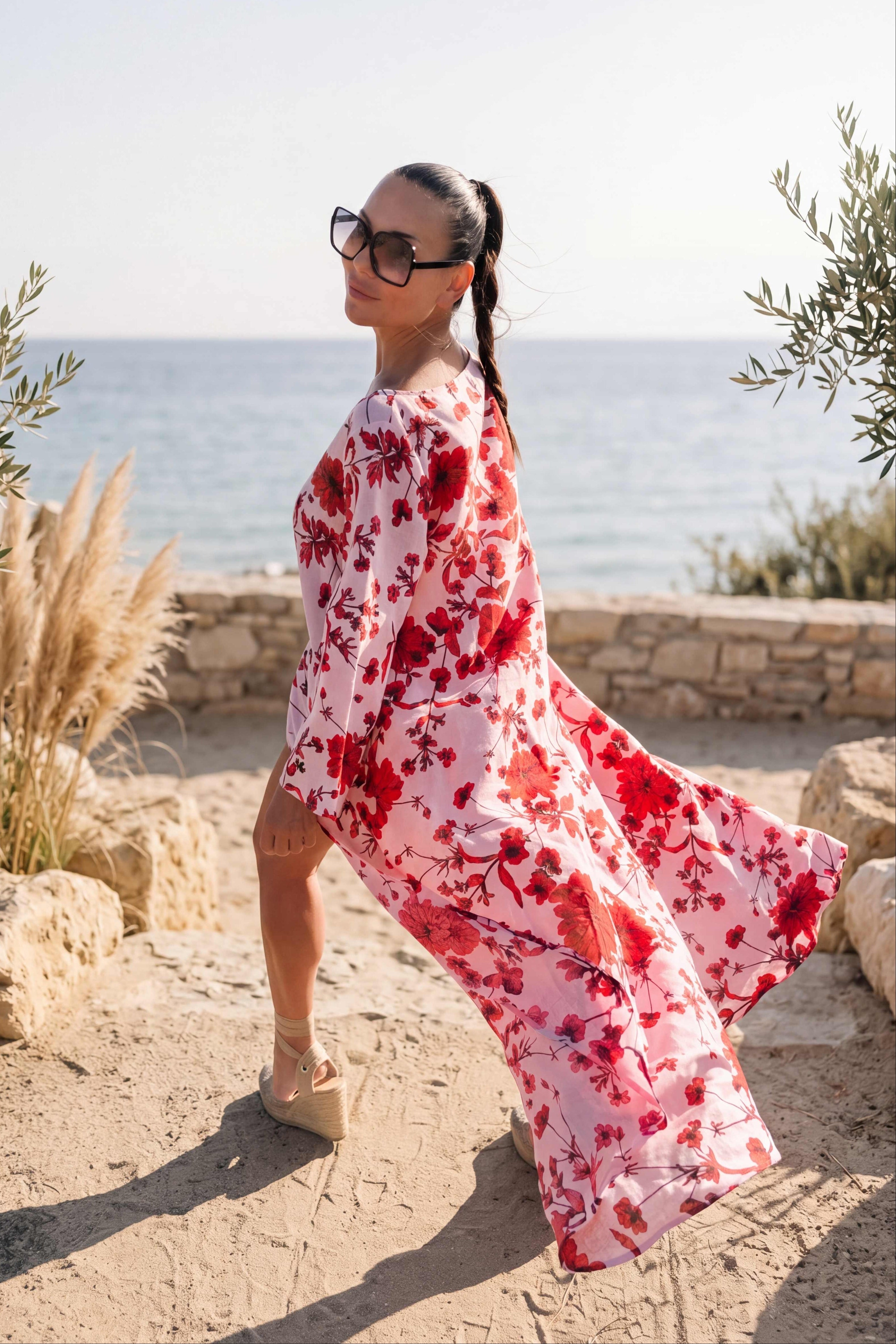 Woman in a red and white floral dress standing by the ocean.