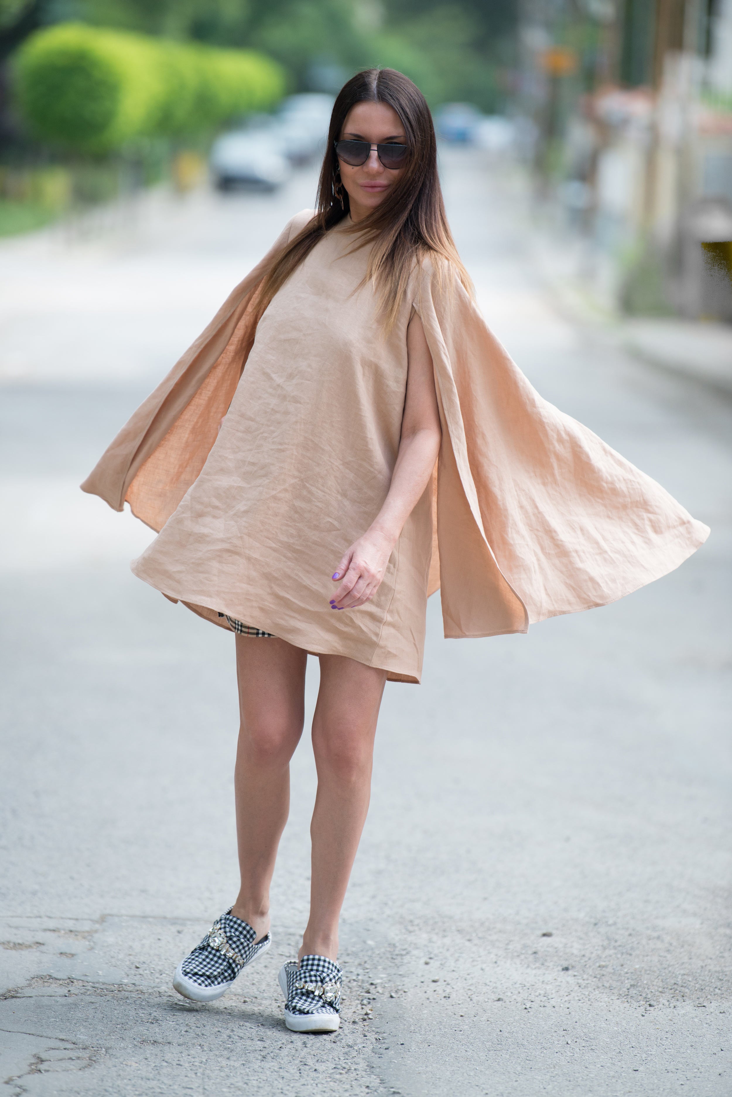 Woman wearing a beige linen dress with a cape effect on a street.