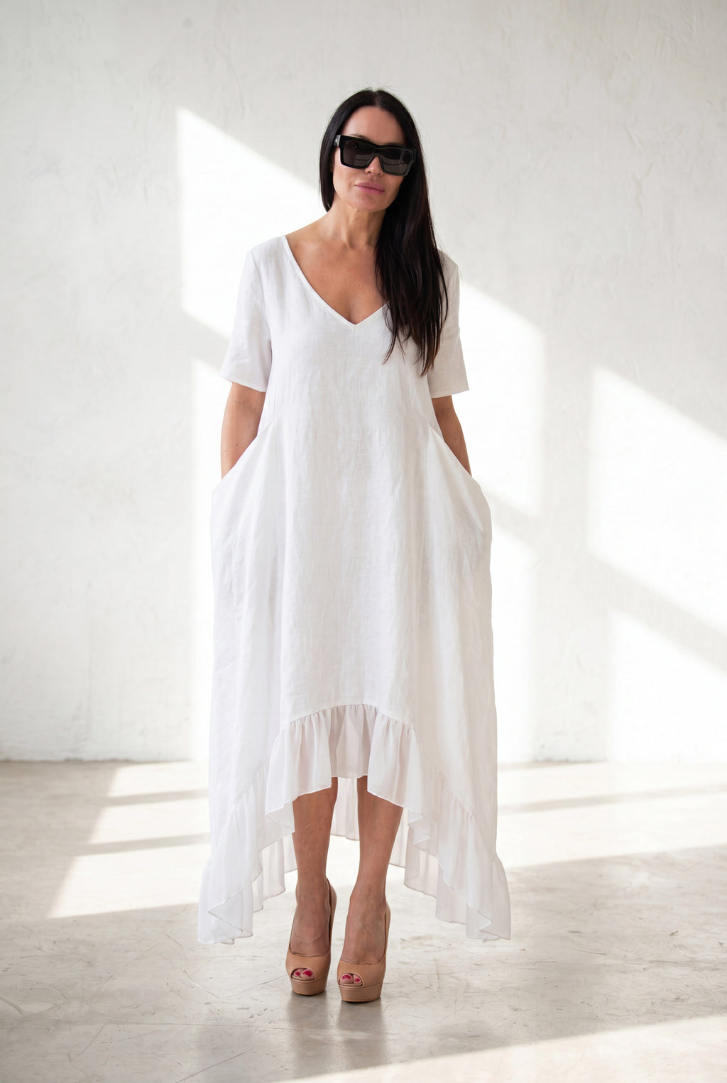 Woman wearing a white linen dress with a high-low hem on a white background