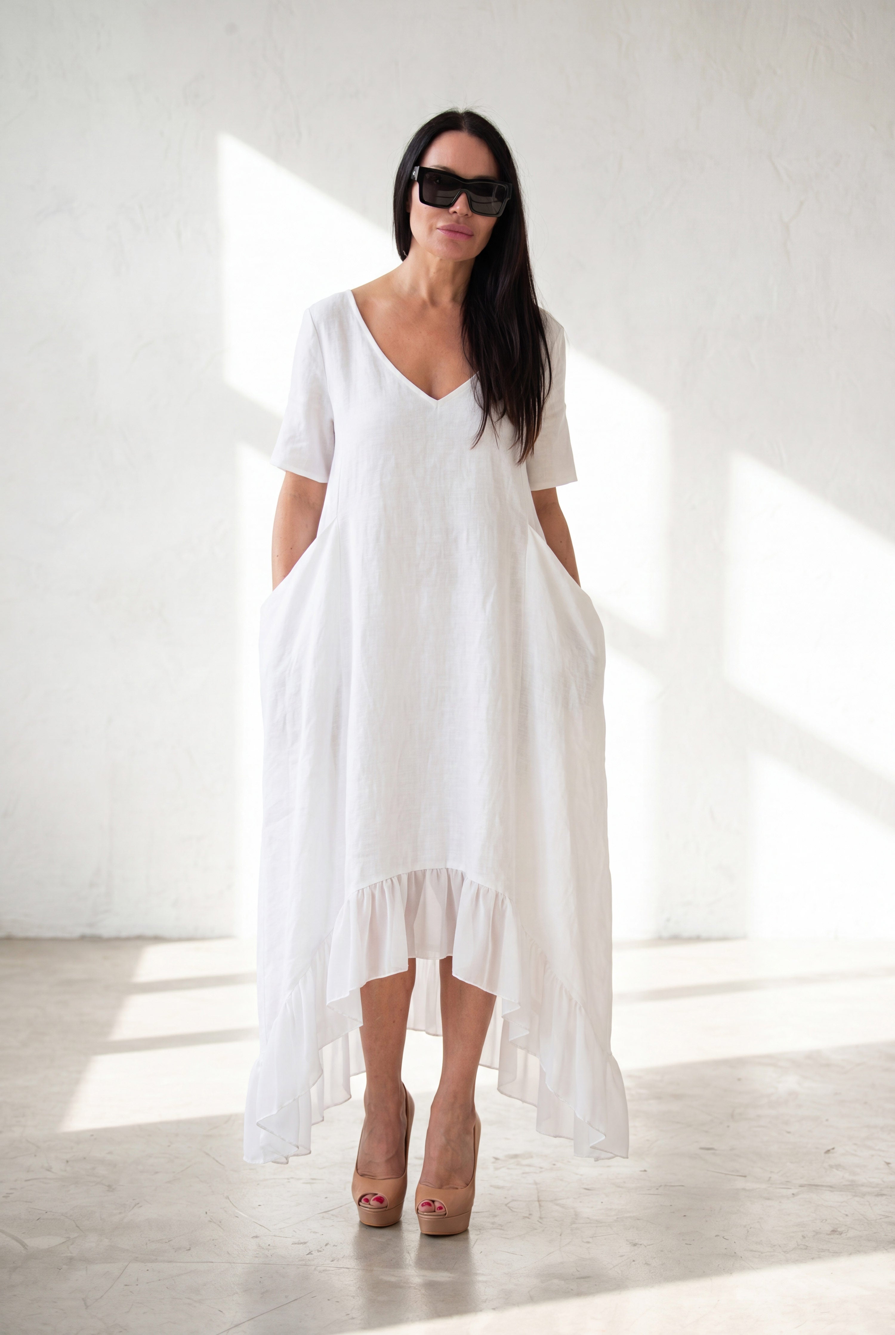 Woman wearing a white linen dress with a high-low hem on a white background