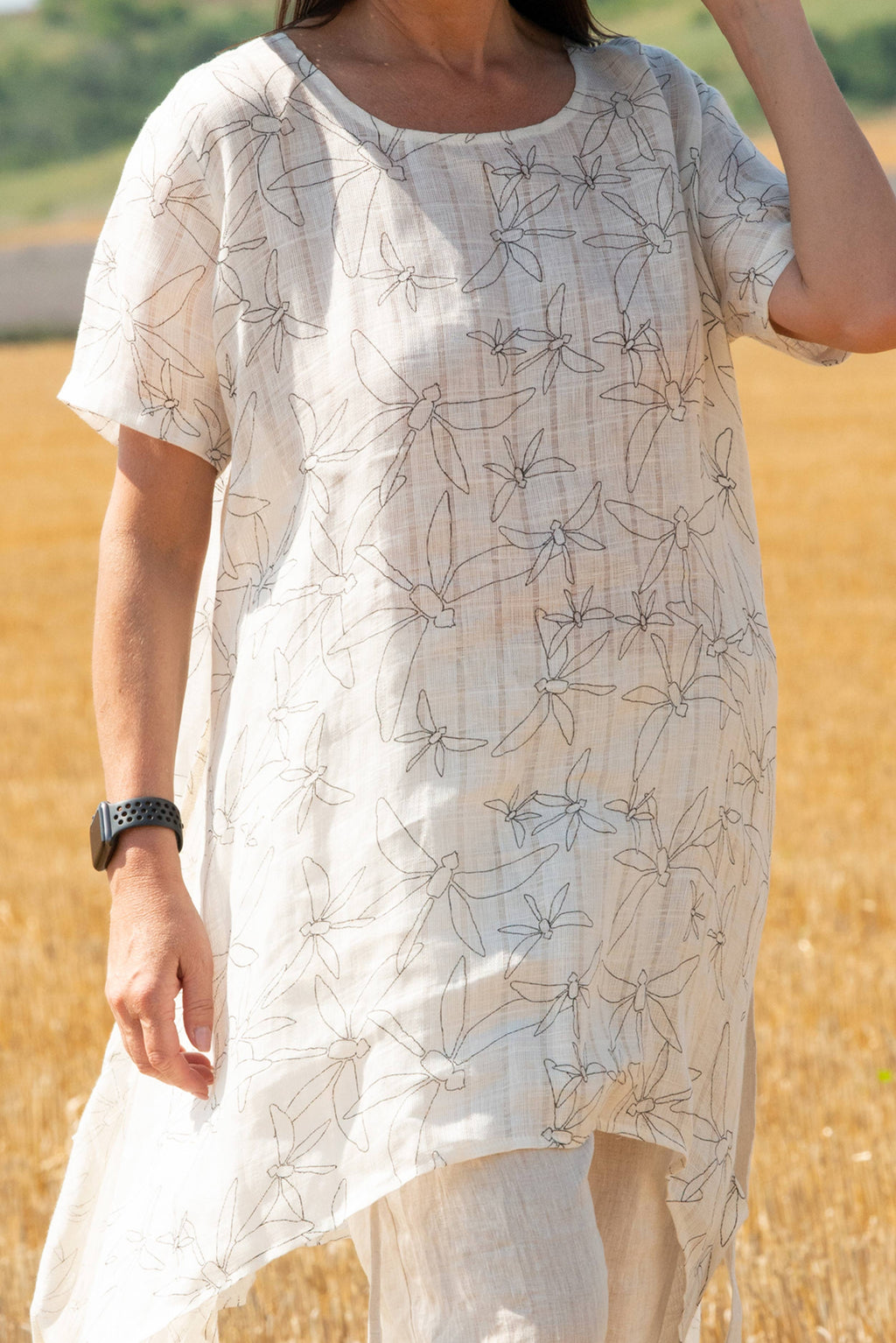 Person wearing a white dress with black floral pattern in a field