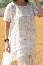 Person wearing a white dress with black floral pattern in a field