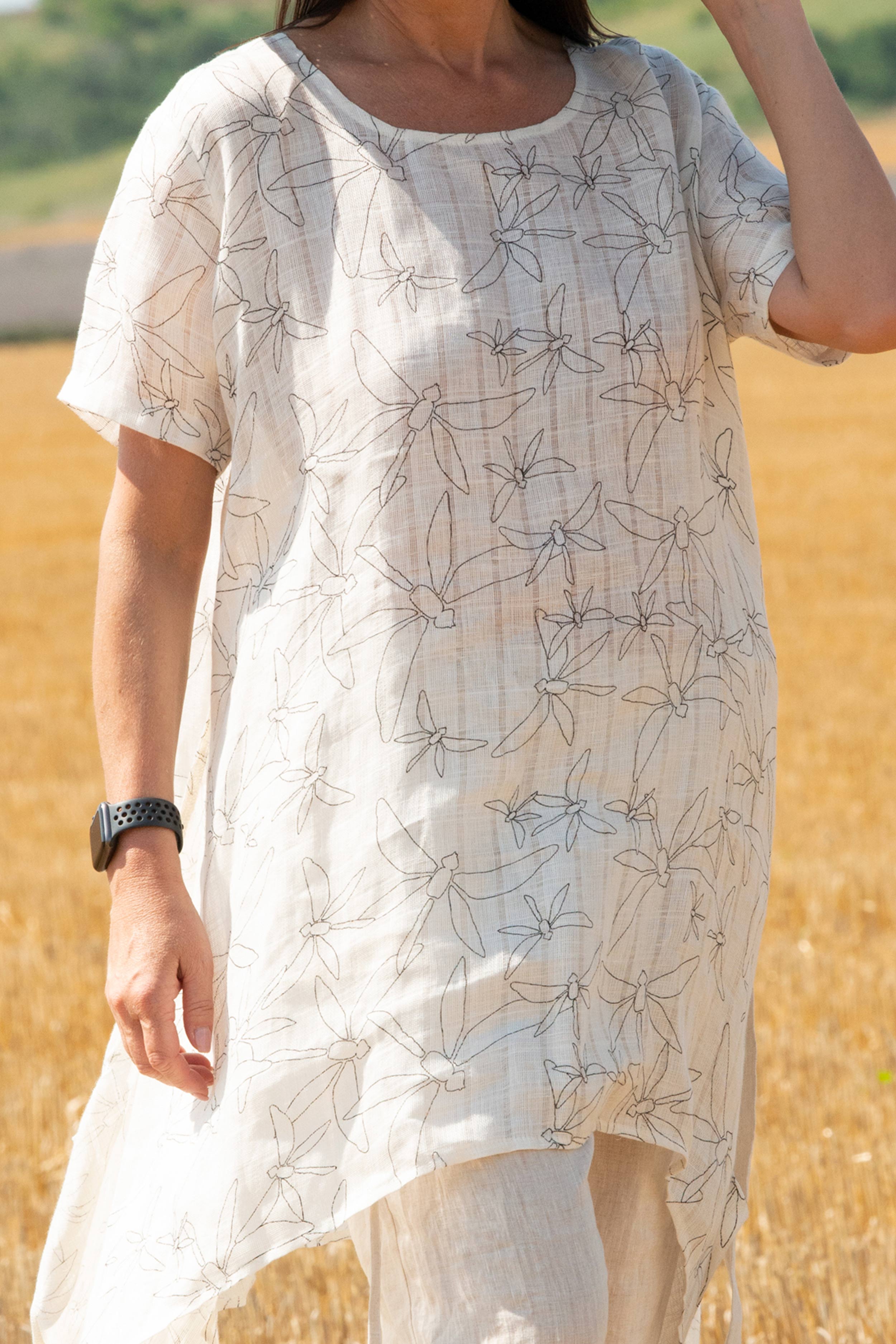 Person wearing a white dress with black floral pattern in a field