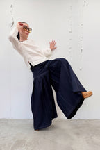 Person wearing a white shirt and navy wide-leg pants against a white wall.