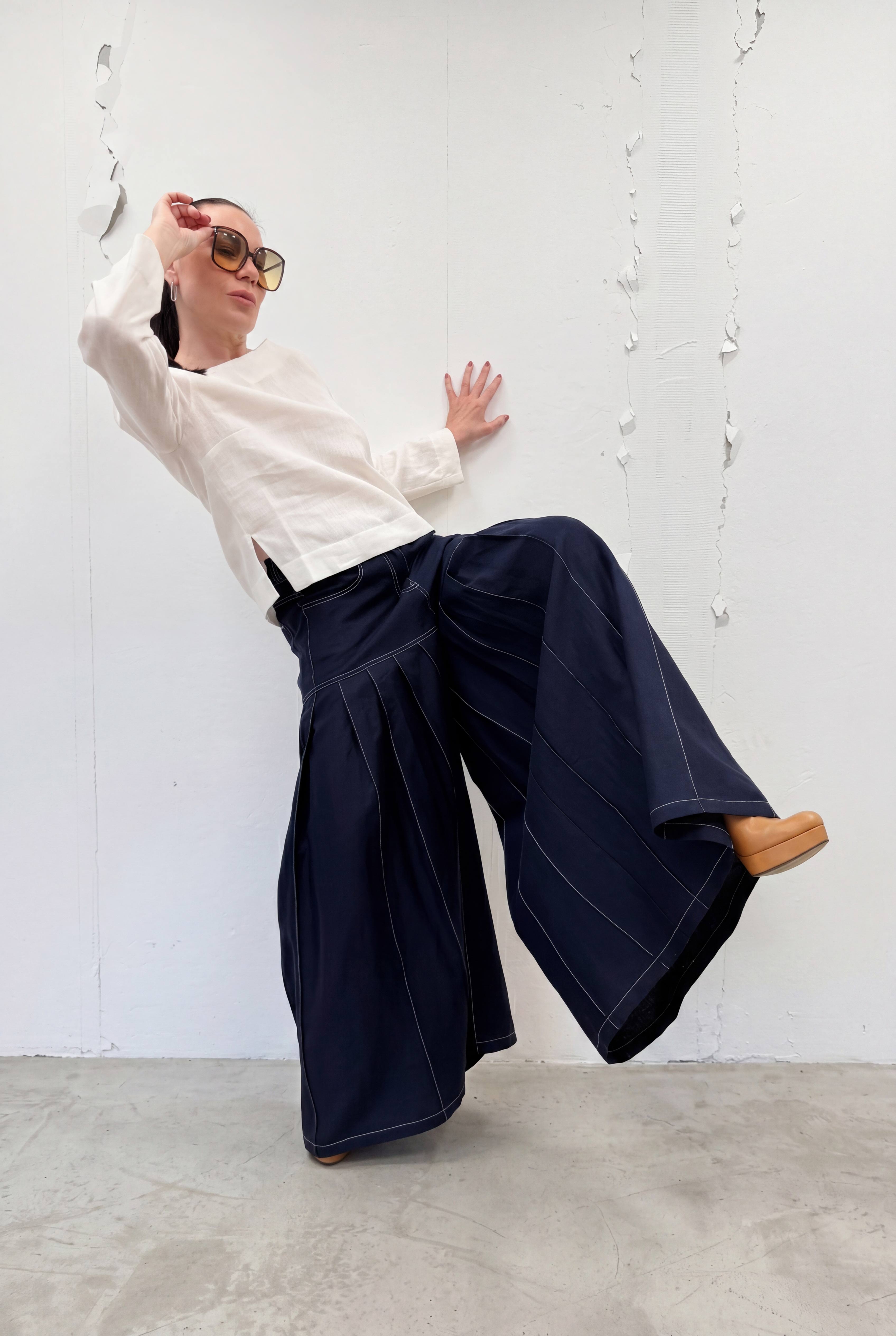 Person wearing a white shirt and navy wide-leg pants against a white wall.