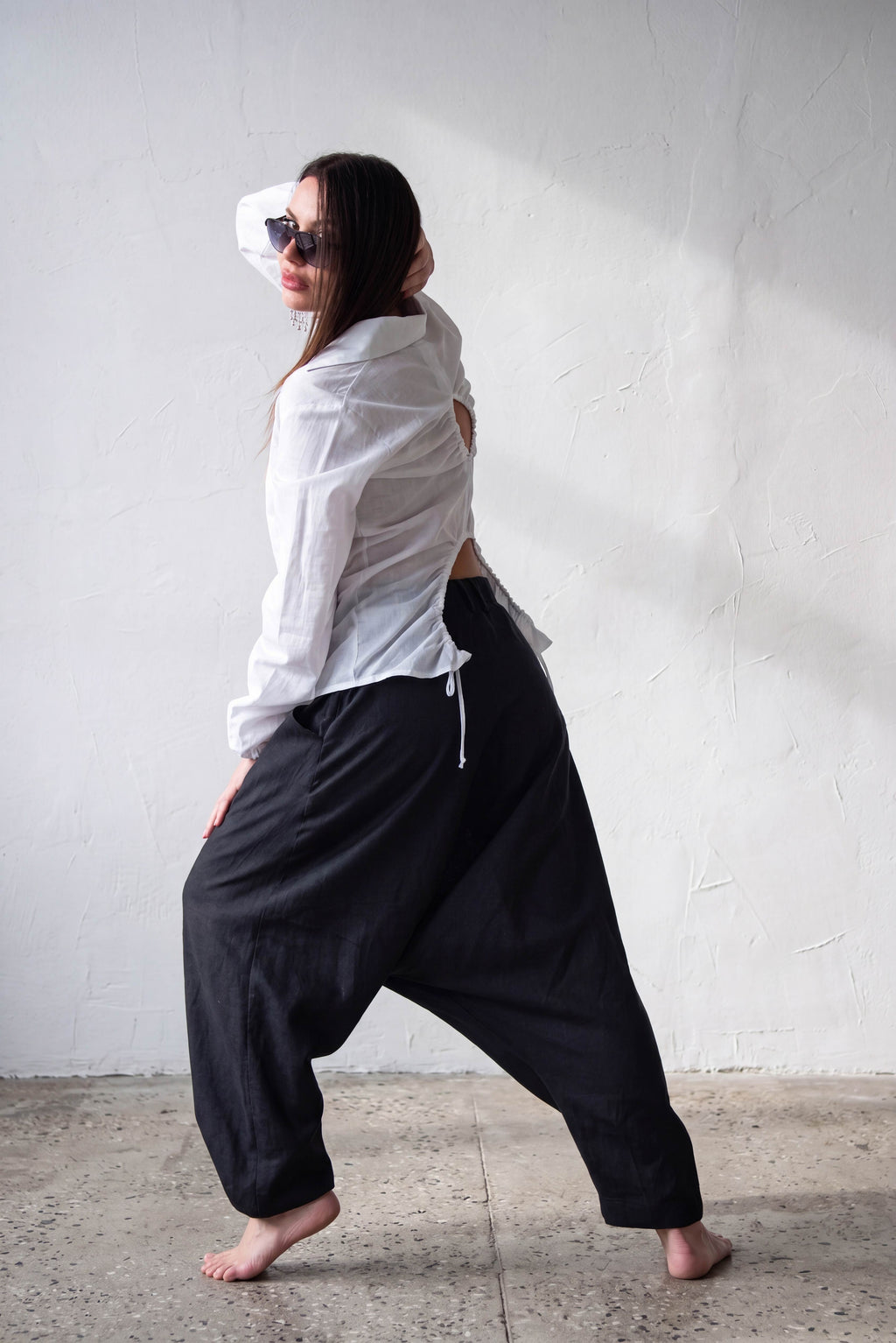 Person wearing a white shirt and black linen harem pants against a plain wall.