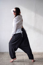 Person wearing a white shirt and black linen harem pants against a plain wall.