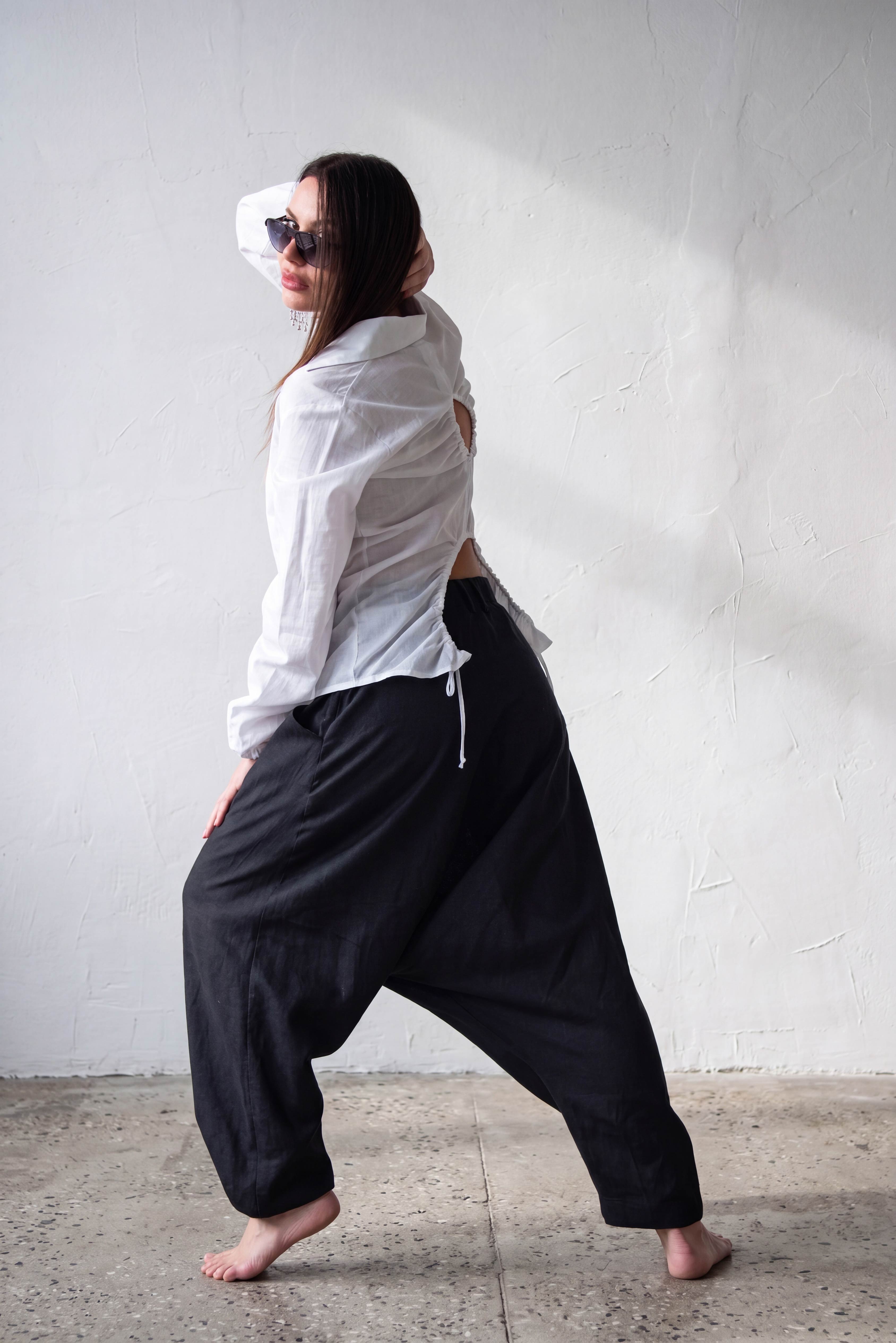 Person wearing a white shirt and black linen harem pants against a plain wall.