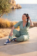 Woman in a green jumpsuit sitting by the sea with blue sneakers.