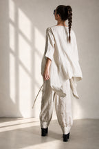 Person wearing a natural linen outfit standing in a room with sunlight casting shadows on the wall.