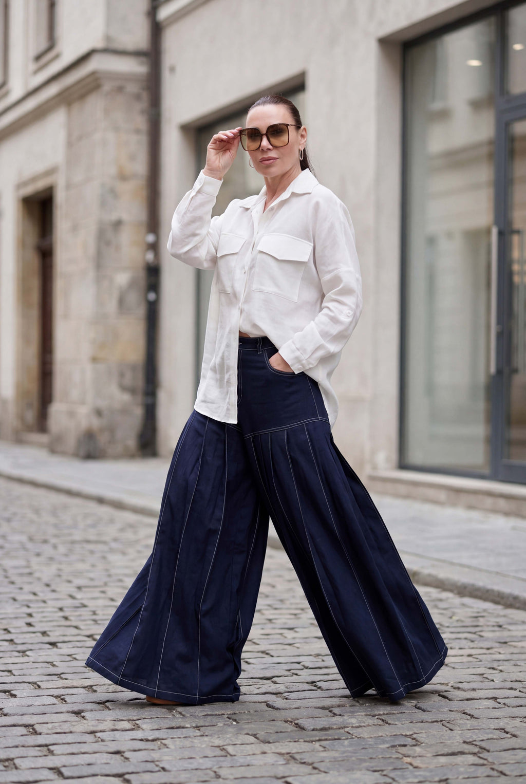 Woman wearing a white blouse and dark blue wide-leg pants on a street.