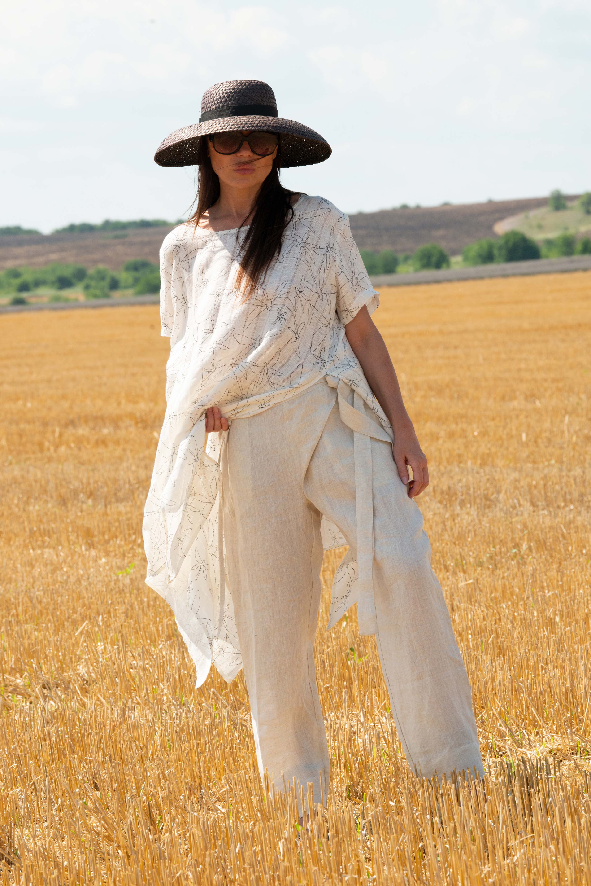 Woman in a white outfit and black hat standing in a golden field
