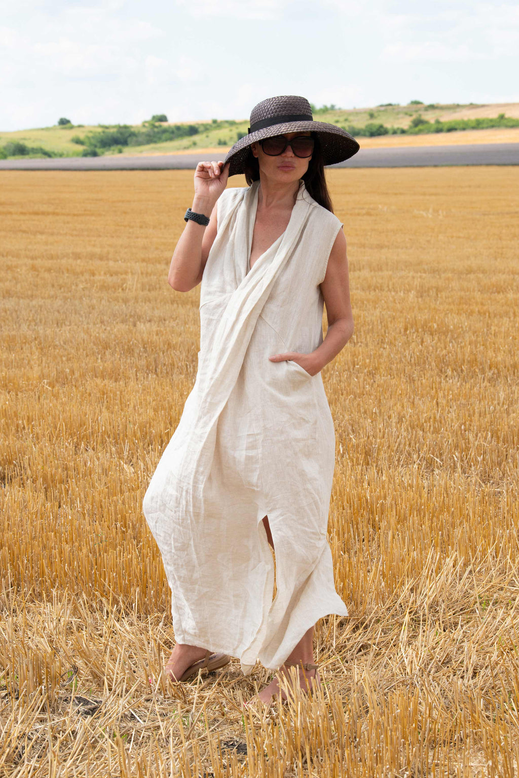 Woman in a natural  dress and black hat standing in a field of golden wheat.