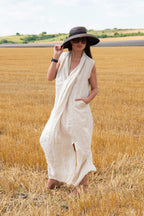 Woman in a natural  dress and black hat standing in a field of golden wheat.