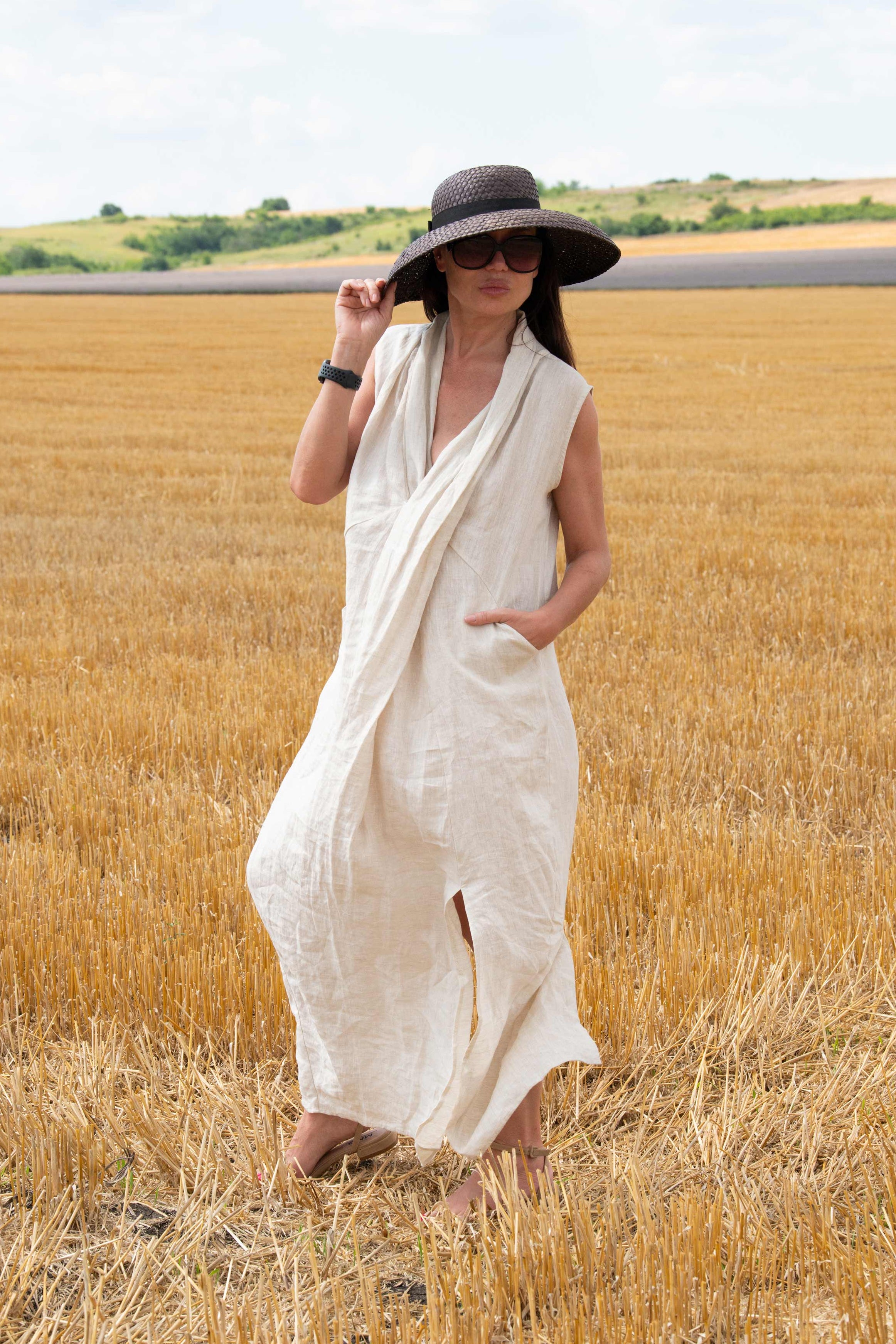 Woman in a natural  dress and black hat standing in a field of golden wheat.
