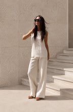 Woman in a beige outfit standing on stone steps against a light-colored wall.
