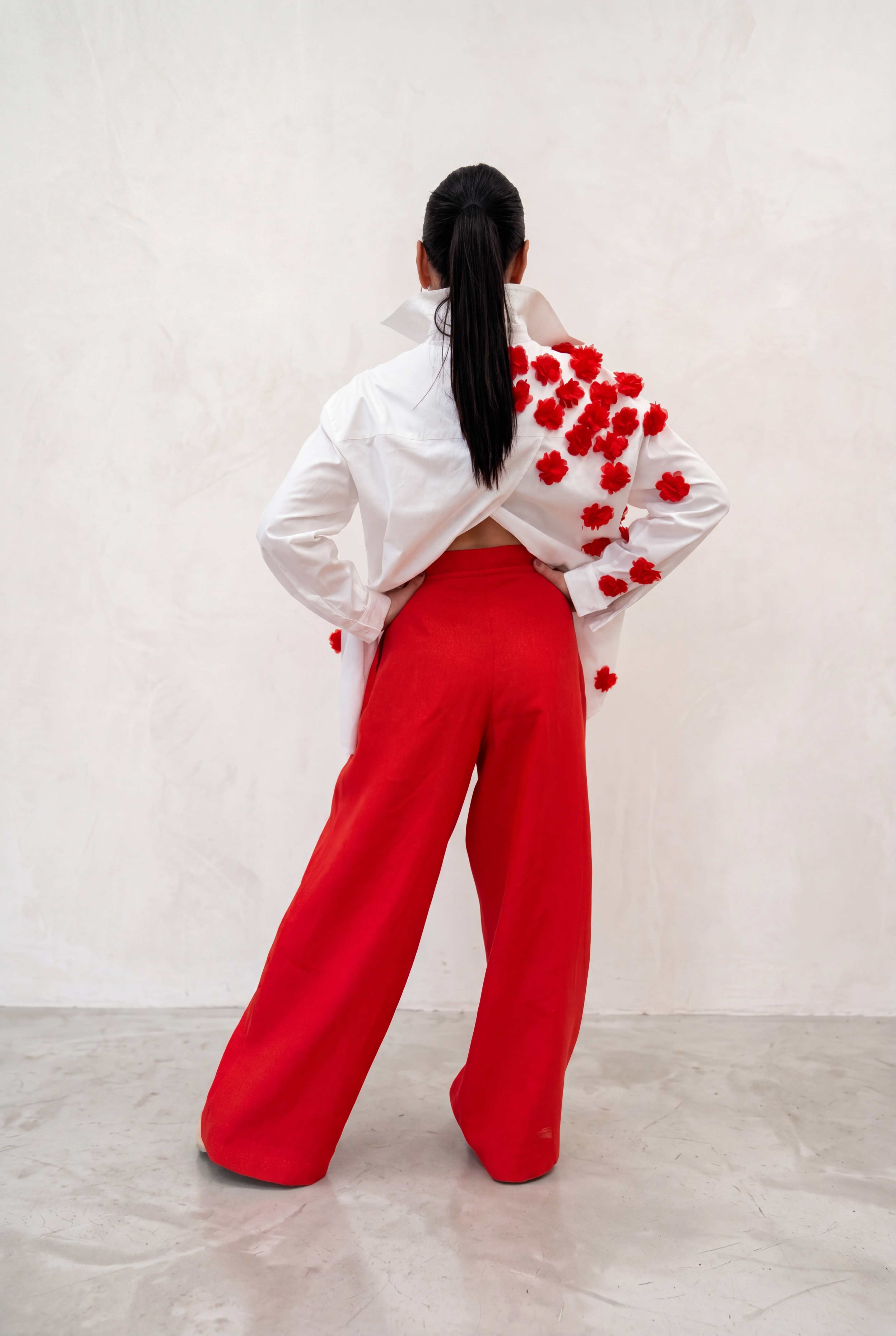 Person wearing a white jacket with red floral patterns and red pants on a plain background