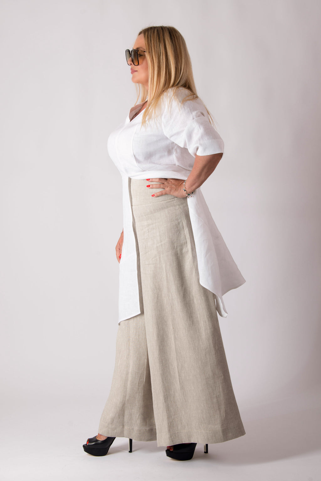 Woman wearing a white blouse and beige wide-leg pants against a white background