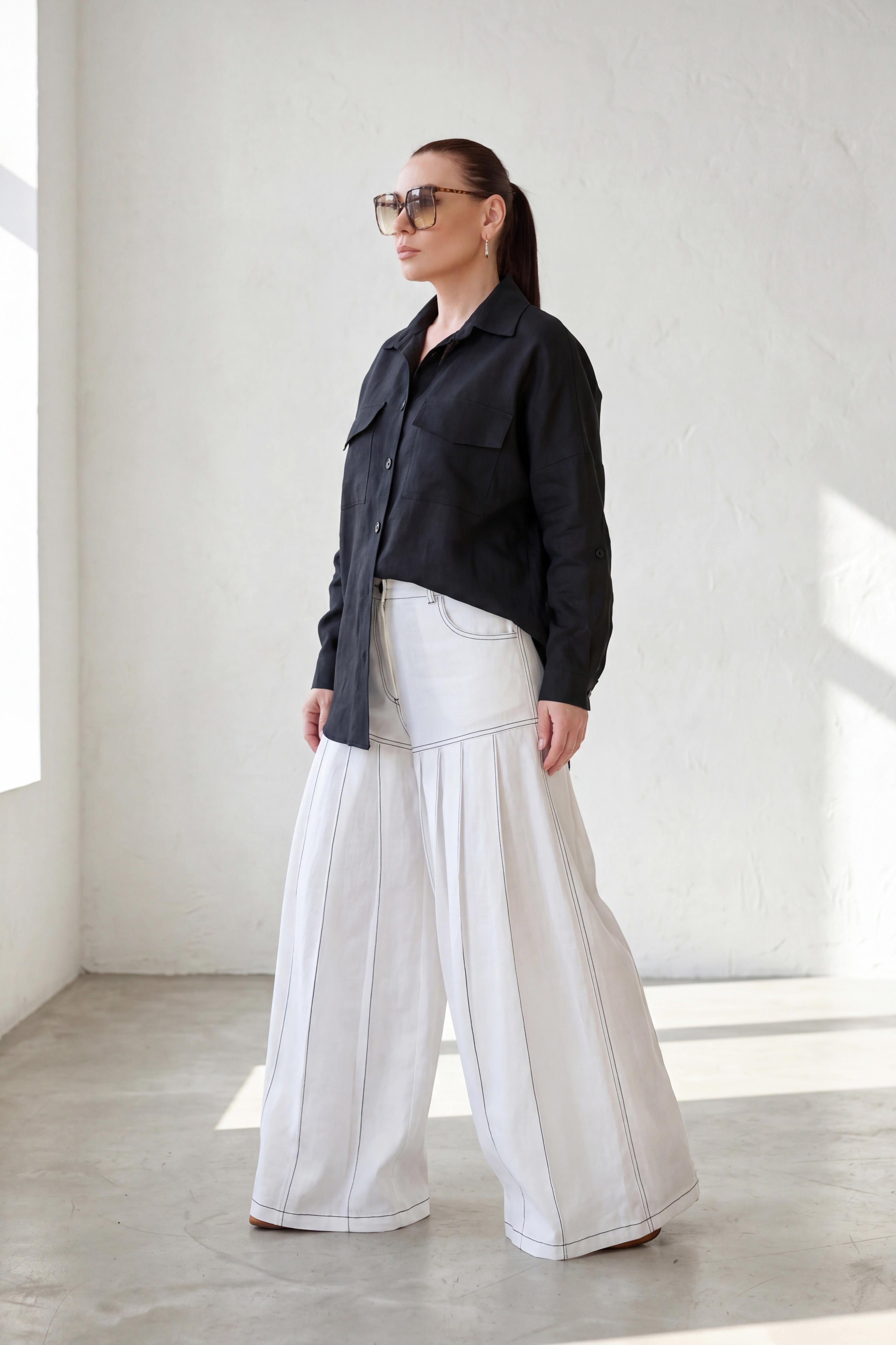 Person wearing a black shirt and white pants in a minimalistic room.