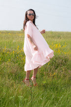 Woman in a pink dress standing in a grassy field with wildflowers.