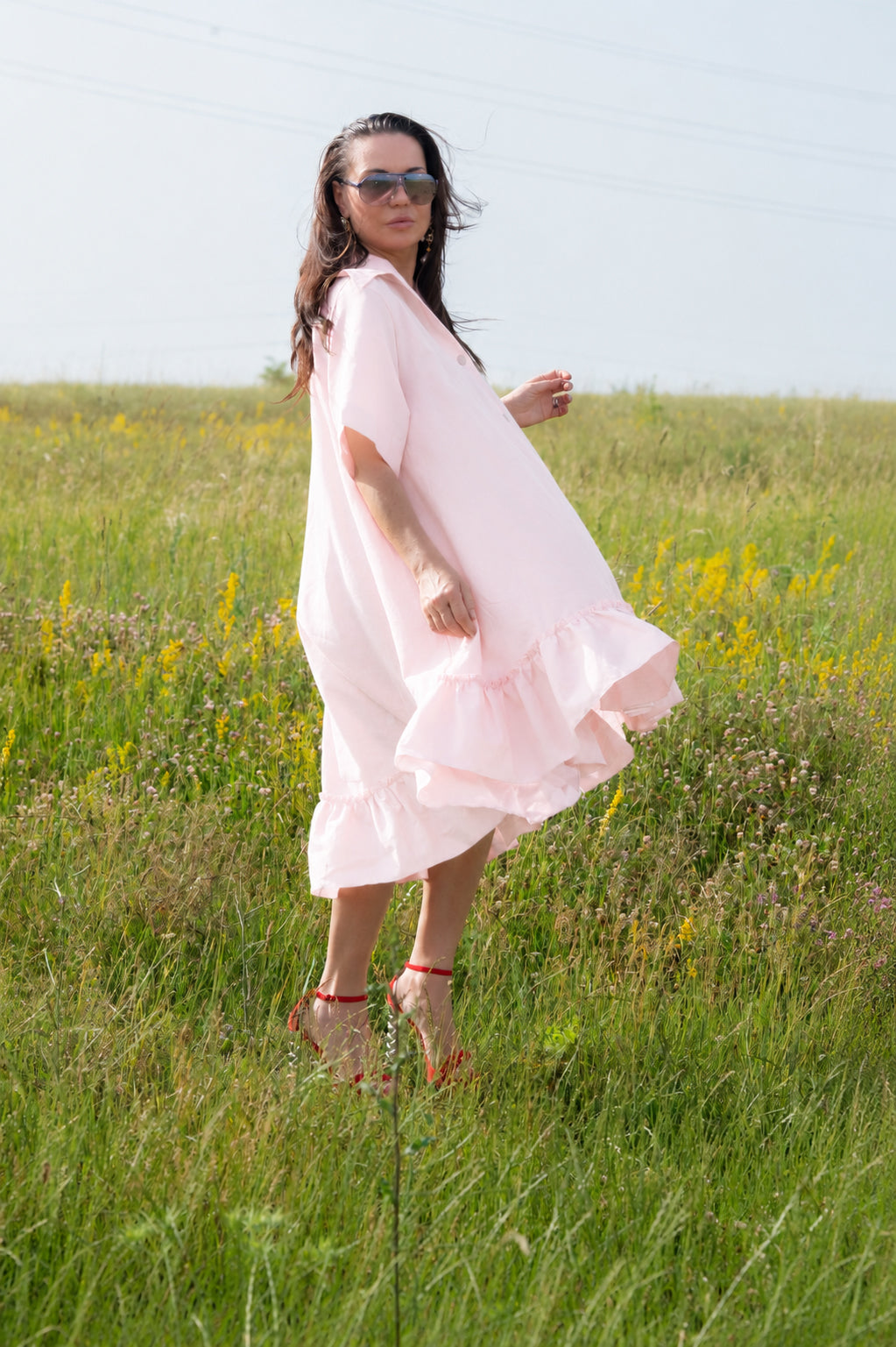 Woman in a pink dress standing in a grassy field with wildflowers.