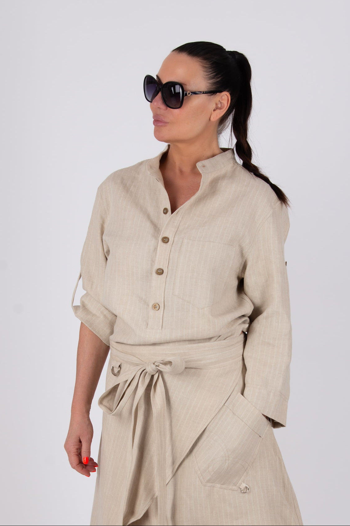 Woman wearing a beige outfit with sunglasses on a white background