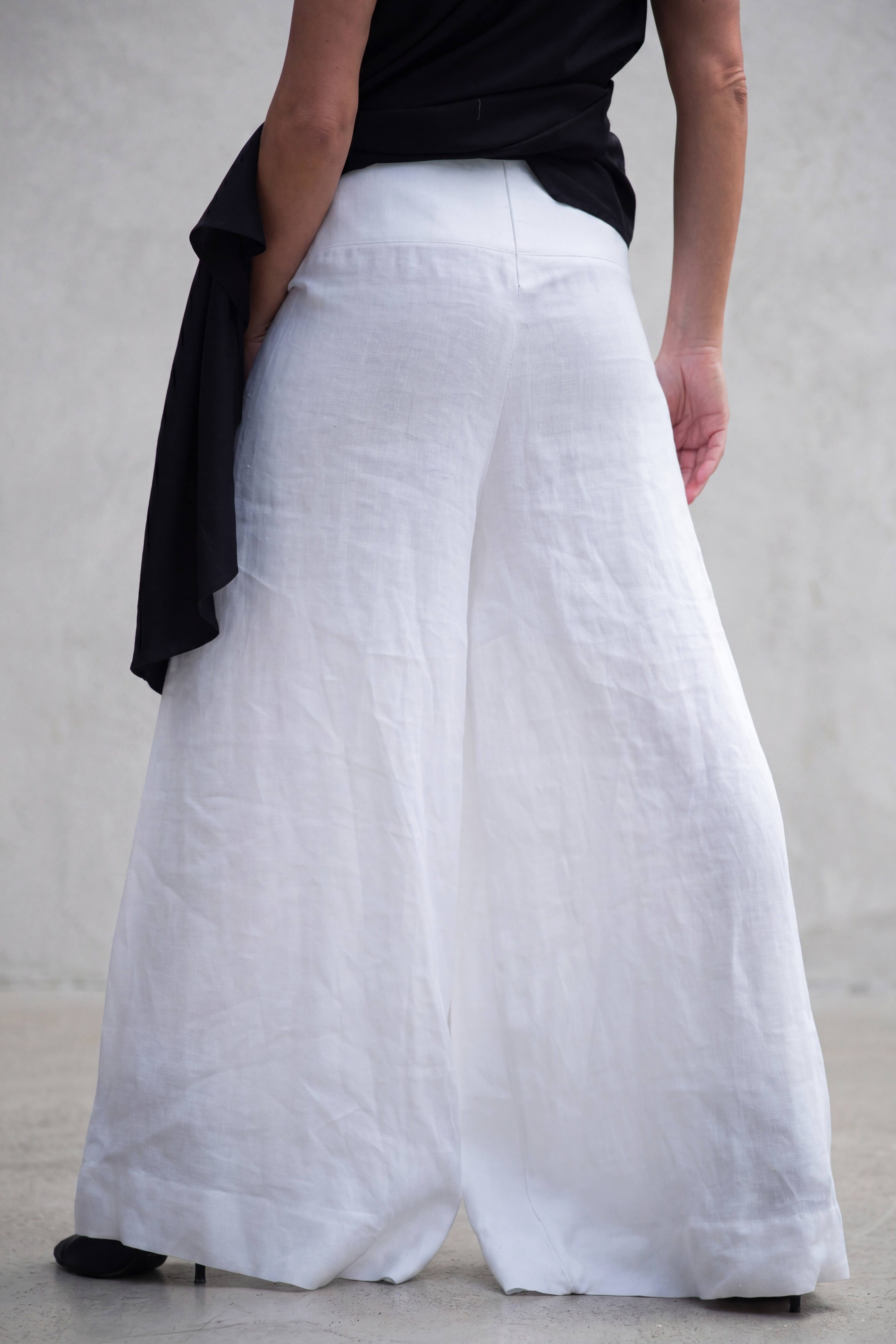 Person wearing white wide-leg pants with a black top on a plain background
